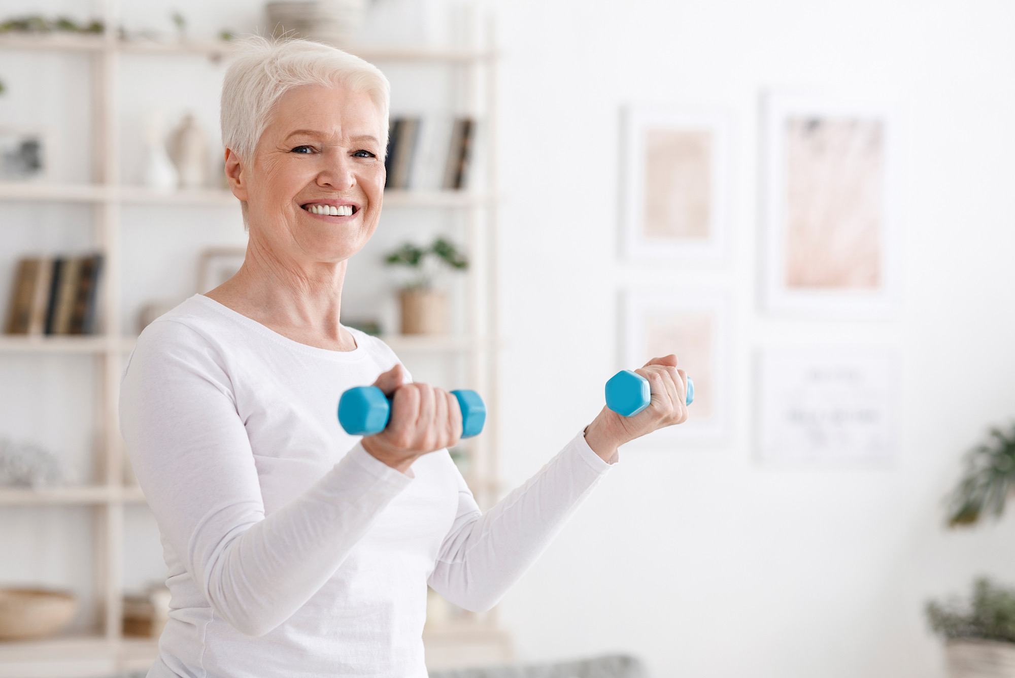 Cheerful senior woman exercising with dumbbells at home, enjoying active healthy lifestyle